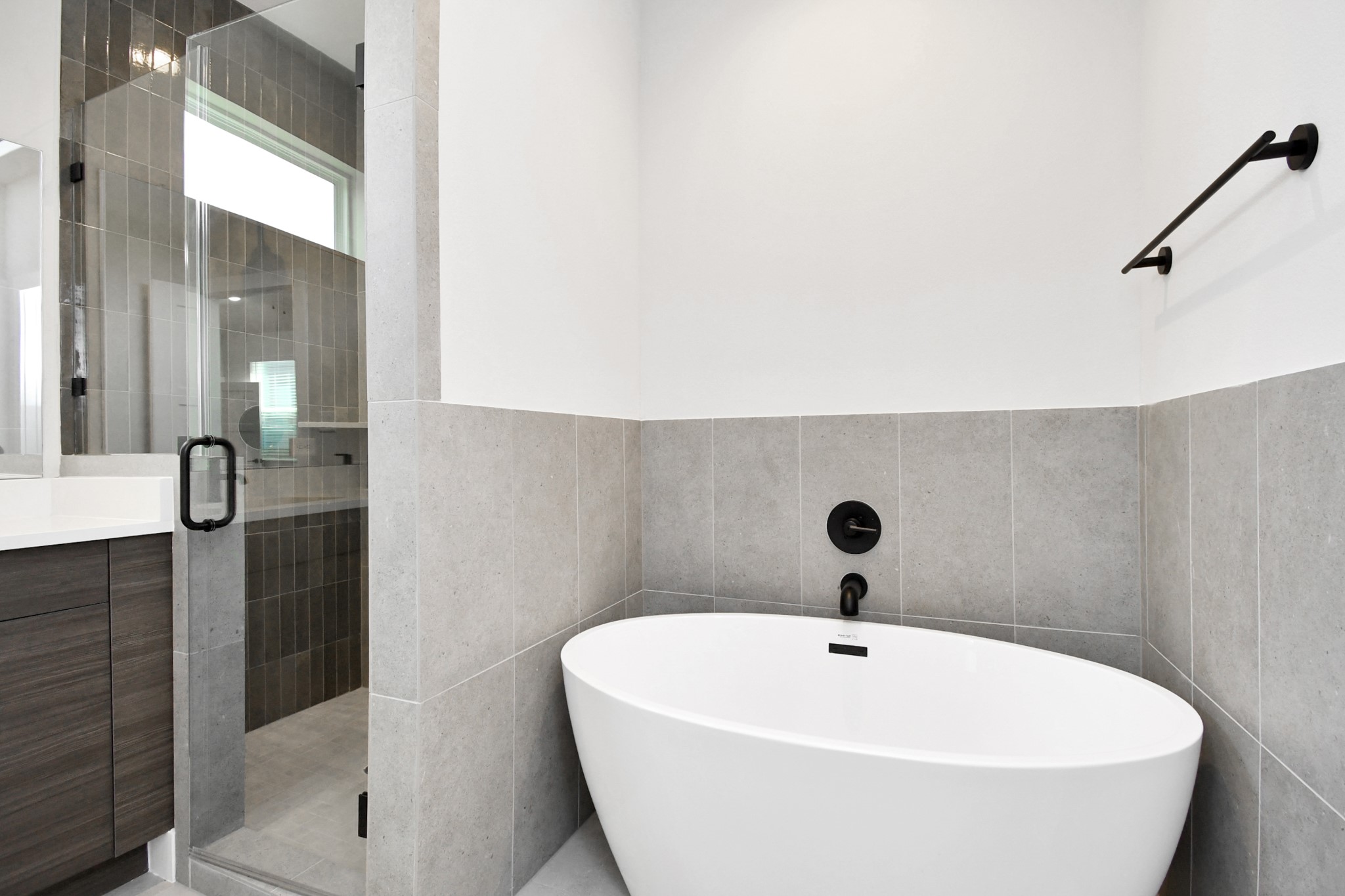 313 Charlock Street Houston, TX 77022 - Photo 21 of 34 This modern bathroom features a sleek freestanding tub, elegant gray tile, a glass-enclosed shower, and contemporary black fixtures, creating a stylish and relaxing space.