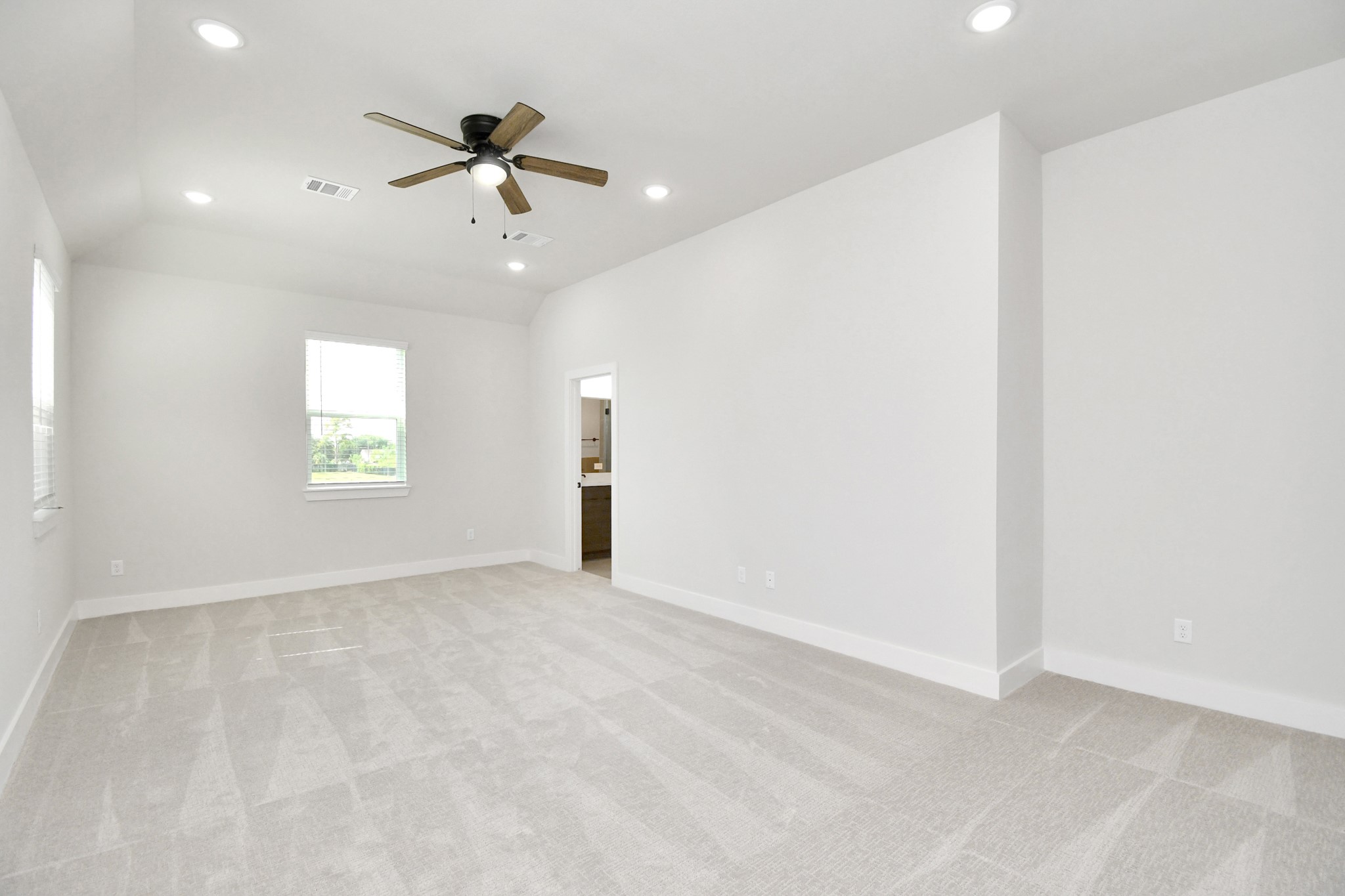 313 Charlock Street Houston, TX 77022 - Photo 24 of 34 Spacious, bright room with neutral carpeting and white walls. Features recessed lighting, a ceiling fan, and two windows for natural light. An open doorway leads to an adjacent room, possibly a bathroom.