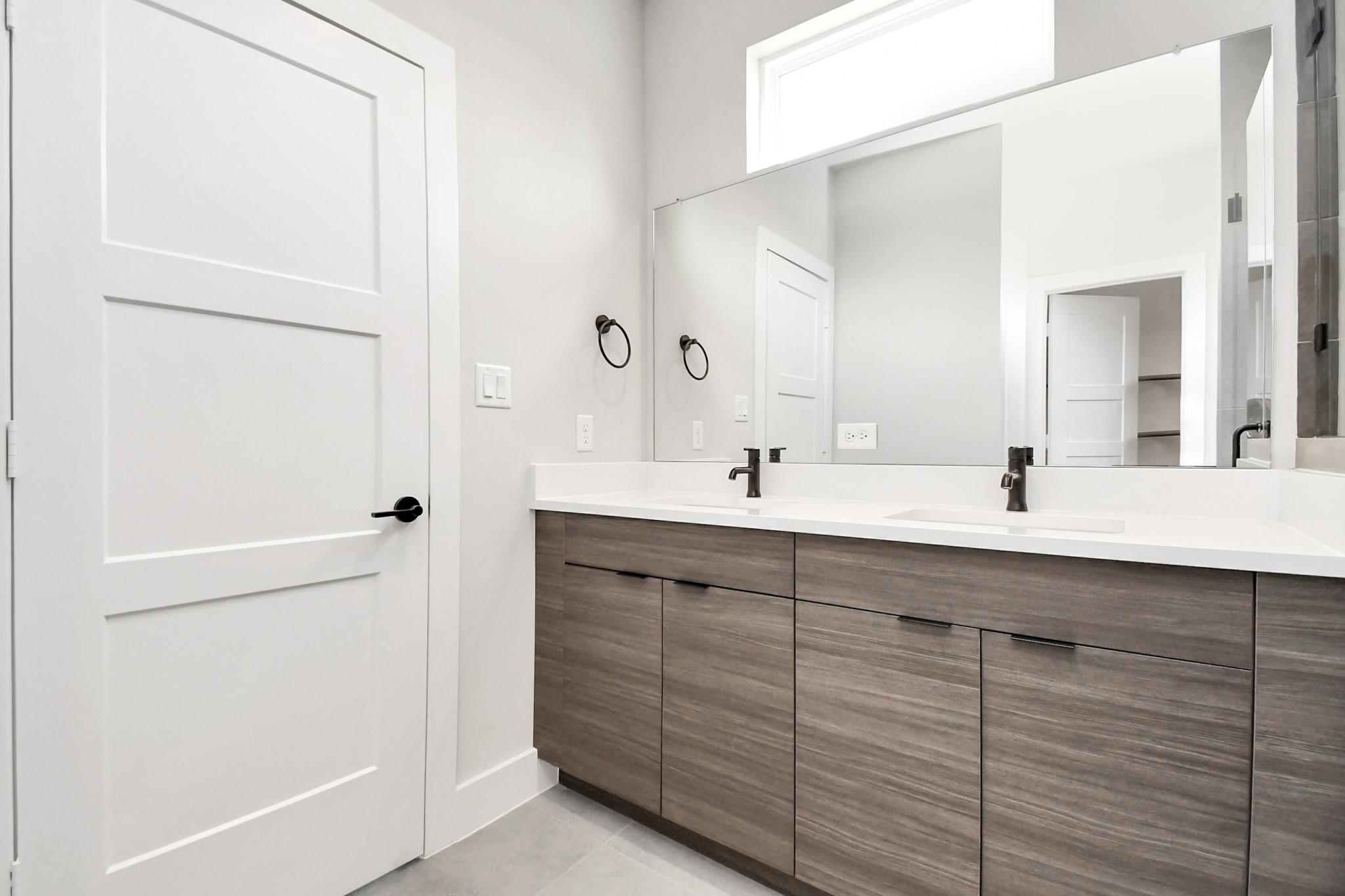 313 Charlock Street Houston, TX 77022 - Photo 25 of 34 This bathroom features a modern design with a large mirror and dual sinks set in a sleek vanity with wood-finish cabinets. The space is well-lit with neutral walls and a minimalist style, creating a clean and inviting atmosphere.