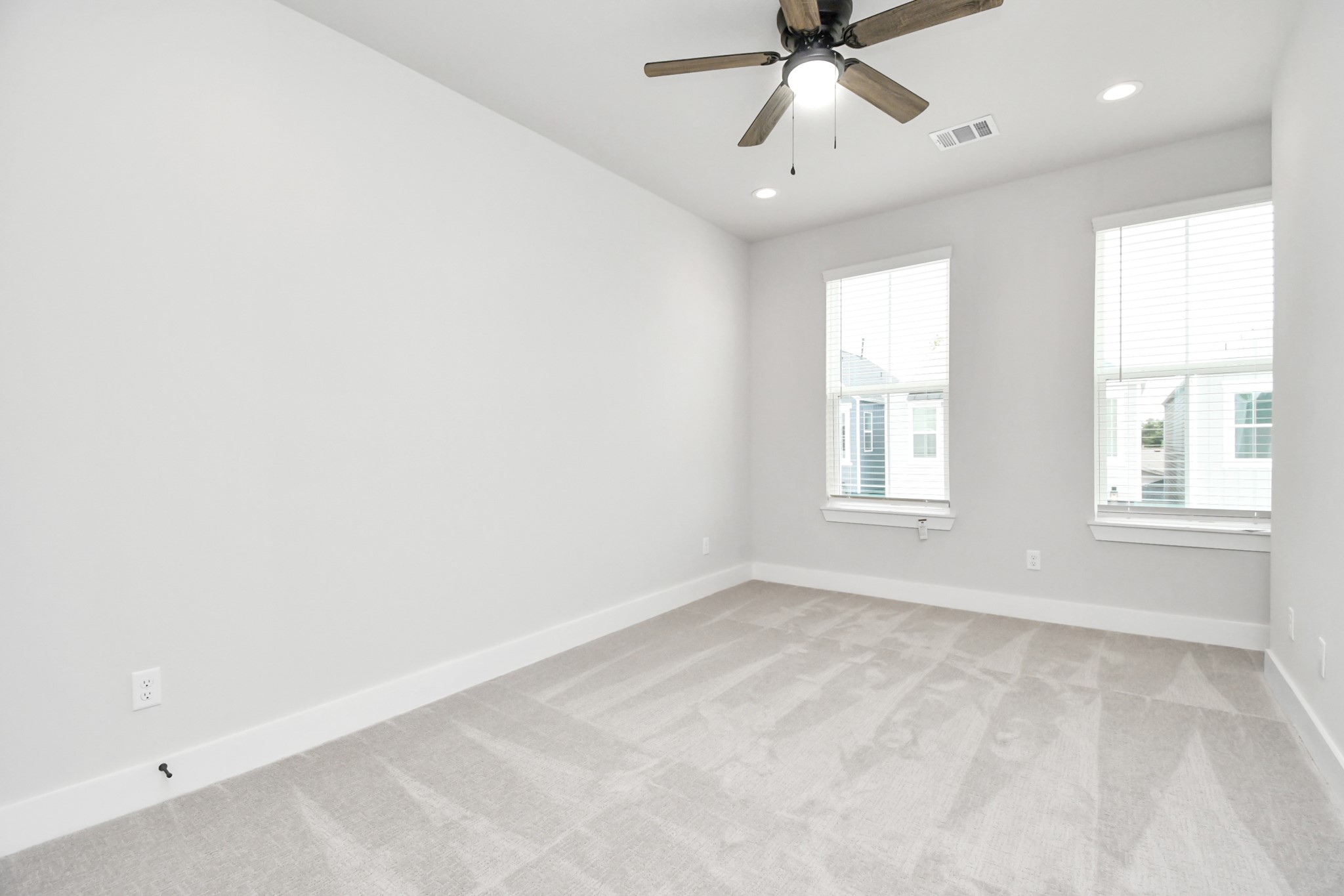 313 Charlock Street Houston, TX 77022 - Photo 26 of 34 Bright, spacious room with neutral walls and carpet, featuring two large windows for natural light and a ceiling fan for comfort.