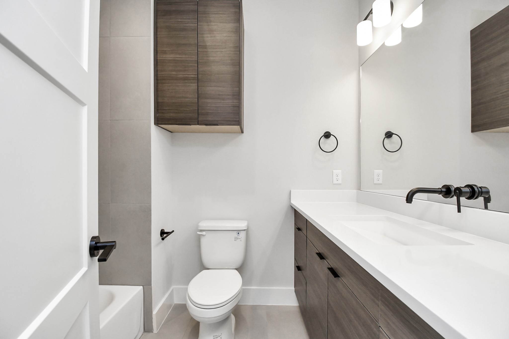 313 Charlock Street Houston, TX 77022 - Photo 27 of 34 This modern bathroom features sleek cabinetry, a large mirror, and a contemporary sink with wall-mounted faucet. It offers ample storage, a toilet, and a partial view of a bathtub. Clean lines and neutral tones create a sophisticated look.