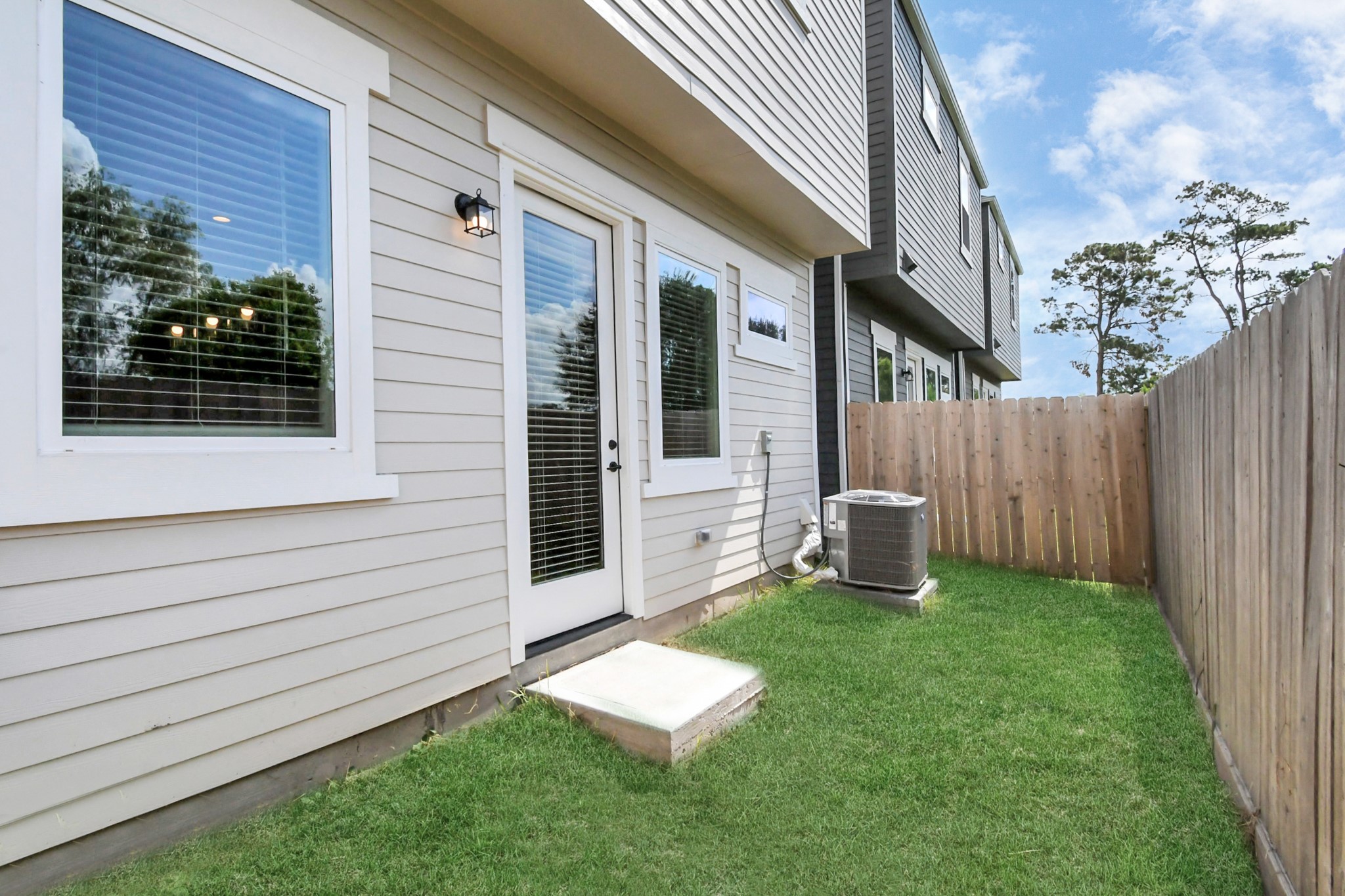 313 Charlock Street Houston, TX 77022 - Photo 28 of 34 This photo shows a small, fenced backyard with a grassy area and an exterior view of a modern townhouse. It includes large windows, a glass door, and an air conditioning unit, providing a cozy outdoor space.