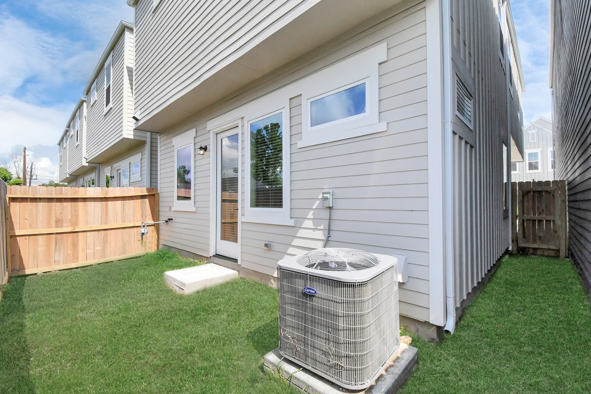 313 Charlock Street Houston, TX 77022 - Photo 30 of 34 This photo shows the exterior of a townhouse with light-colored siding, a small fenced backyard, and an air conditioning unit. The area is well-maintained with green grass, and there is a glass door leading inside.