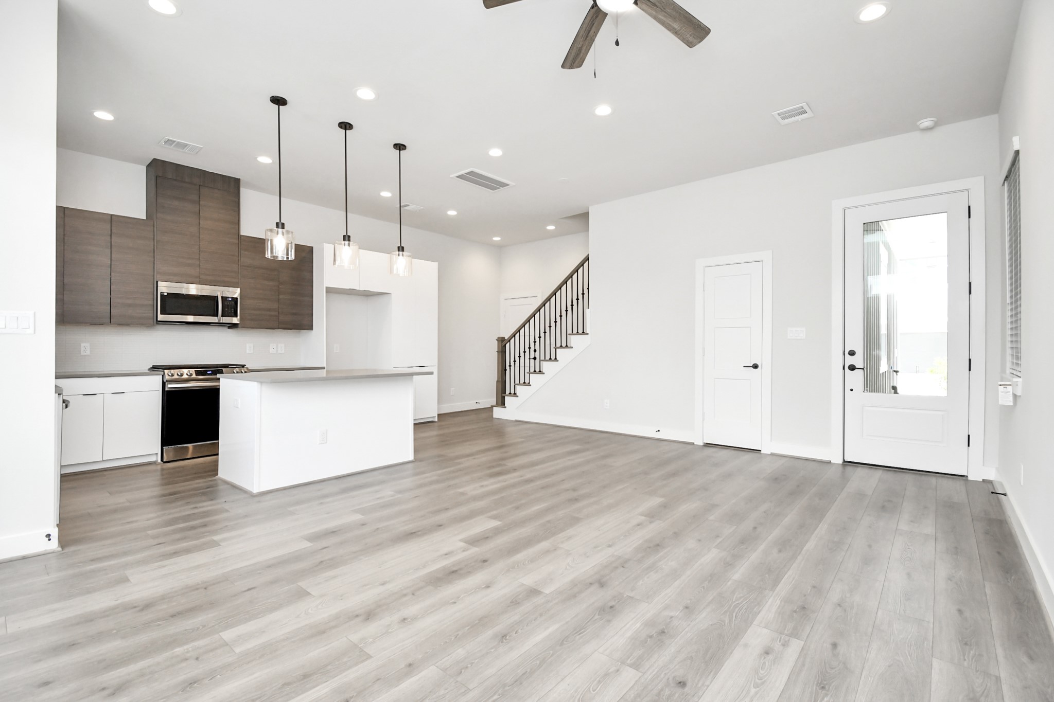 313 Charlock Street Houston, TX 77022 - Photo 3 of 34 This photo showcases a modern open-concept living space with a sleek kitchen featuring stainless steel appliances, a large island, and pendant lighting. The room has light wood flooring, recessed lighting, and a ceiling fan, with a staircase leading to the upper level.