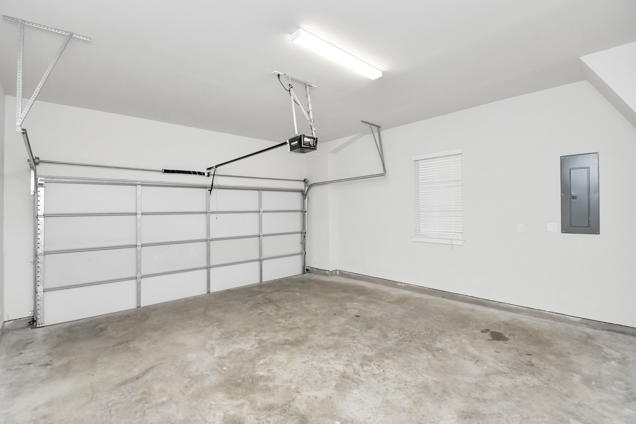 313 Charlock Street Houston, TX 77022 - Photo 31 of 34 This photo shows a clean, spacious garage with a concrete floor, overhead lighting, and a large automatic garage door. A window and electrical panel are also present.