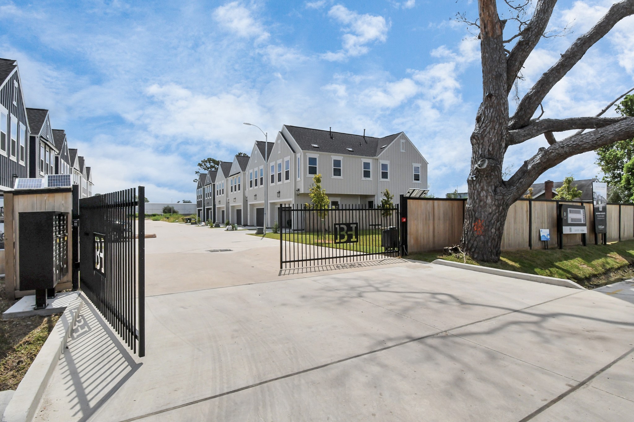 313 Charlock Street Houston, TX 77022 - Photo 32 of 34 This photo shows a modern townhouse community with a gated entrance. The buildings have a clean, contemporary design with multiple units. The area appears well-maintained, and there's a large tree near the entrance, adding some natural charm.