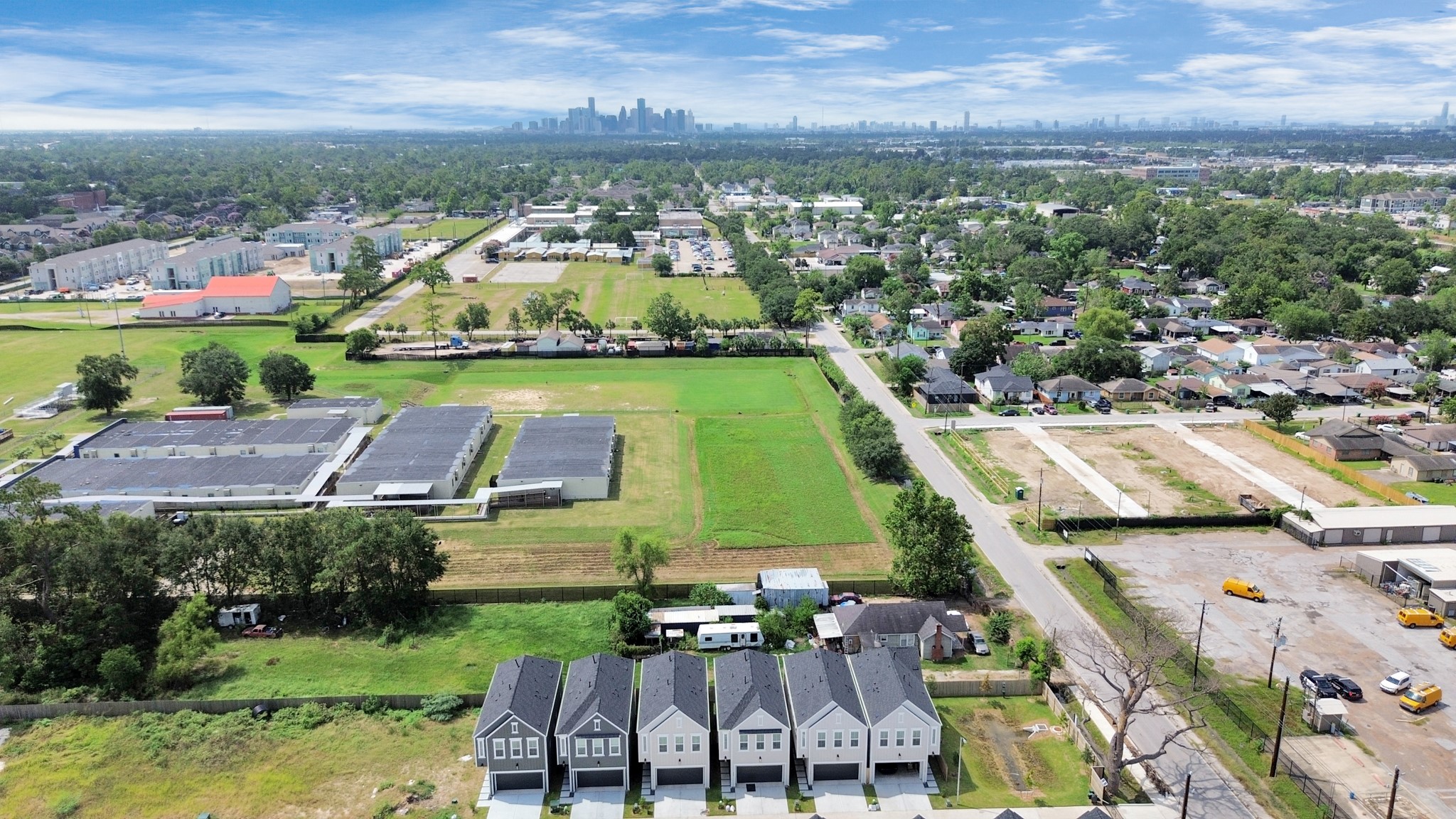 313 Charlock Street Houston, TX 77022 - Photo 34 of 34 This aerial photo shows a suburban neighborhood with new, modern homes in the foreground. The area is green and spacious, with a mix of residential and commercial buildings. The city skyline is visible in the distance, offering a blend of suburban calm and urban convenience.