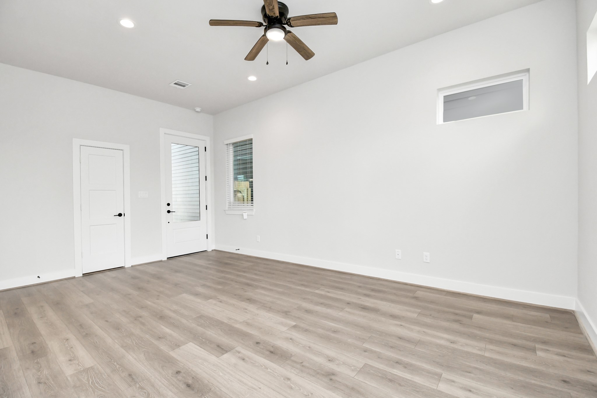 313 Charlock Street Houston, TX 77022 - Photo 4 of 34 Spacious and bright room with light wood flooring, neutral walls, ceiling fan, and recessed lighting. Features a door and window for natural light. Ideal for a modern, airy living space.