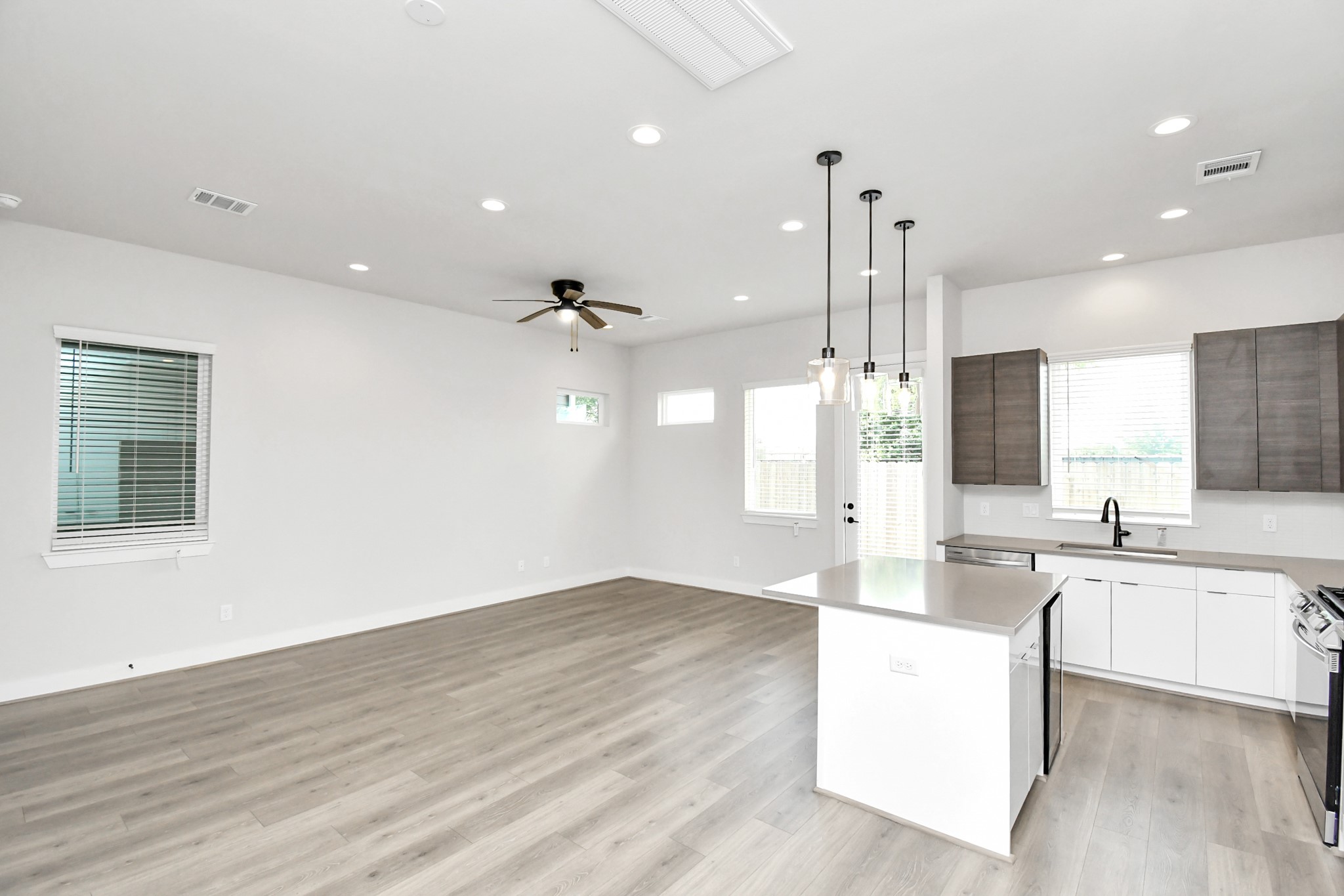 313 Charlock Street Houston, TX 77022 - Photo 6 of 34 This photo showcases a spacious, open-concept living area with modern wood flooring, a ceiling fan, and abundant natural light. The contemporary kitchen features sleek cabinetry, a large island with pendant lighting, and stainless steel appliances, creating an inviting space for cooking and entertaining.