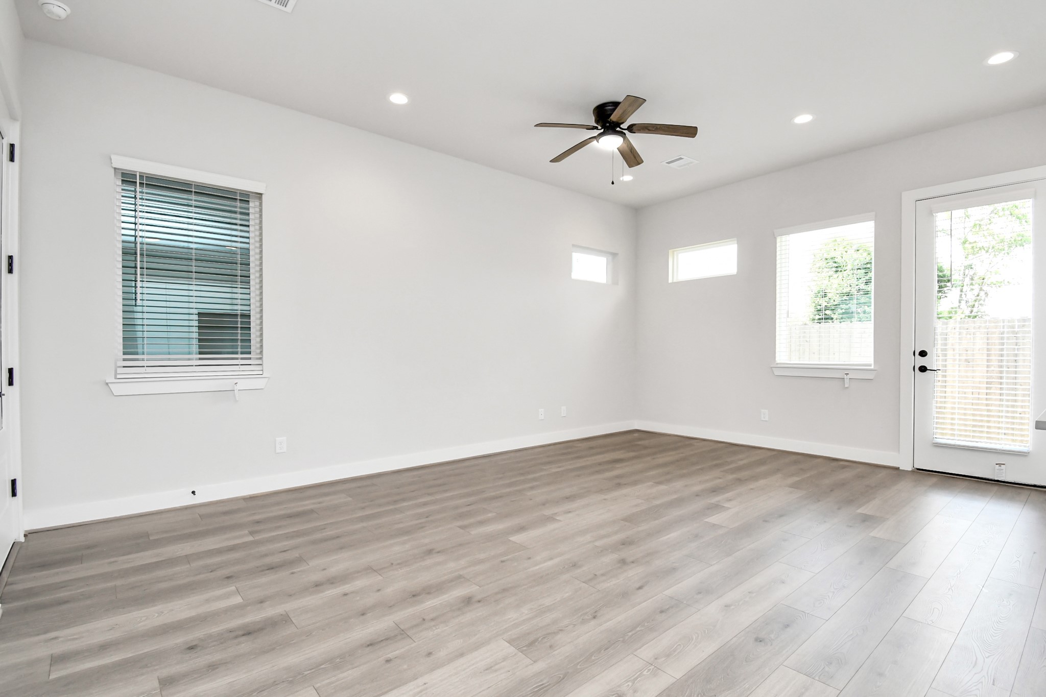 313 Charlock Street Houston, TX 77022 - Photo 7 of 34 Spacious, bright room with wood flooring, neutral walls, recessed lighting, and a ceiling fan. Features multiple windows for natural light and a glass door leading outside.