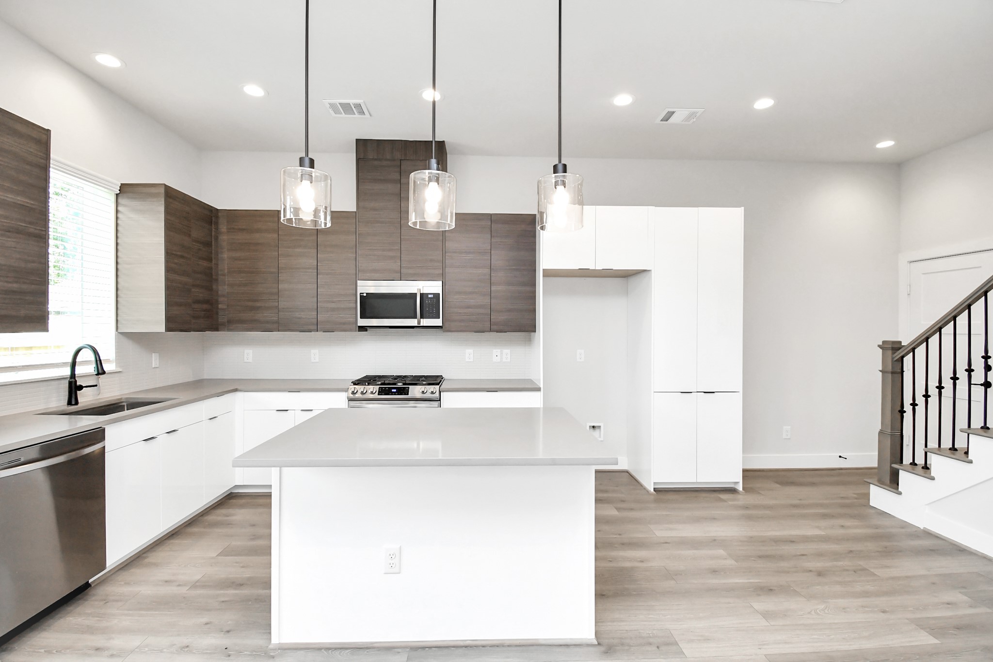 313 Charlock Street Houston, TX 77022 - Photo 8 of 34 This modern kitchen features sleek cabinetry with a mix of wood and white finishes, stainless steel appliances, and a large island with pendant lighting. The open layout and light wood flooring create a bright and inviting space.