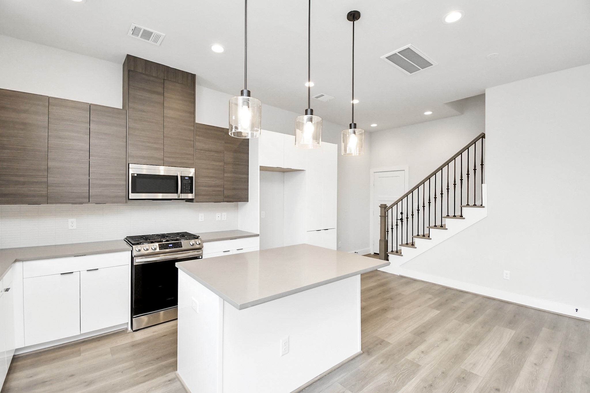 313 Charlock Street Houston, TX 77022 - Photo 9 of 34 This modern kitchen features sleek cabinetry, stainless steel appliances, and a large island with pendant lighting. The open layout flows into a bright living area with wood flooring and a staircase.