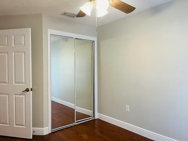 an empty room with wooden floor and fan