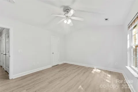 an empty room with wooden floor fan and windows