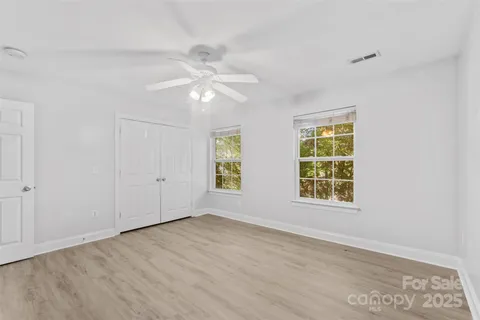 an empty room with wooden floor ceiling fan and windows