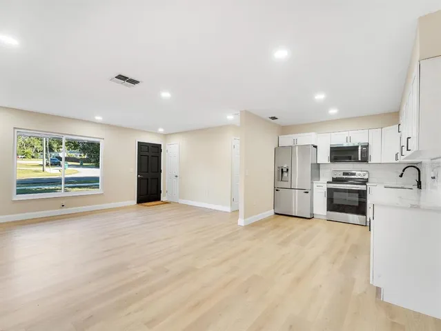 a large white kitchen with stainless steel appliances granite countertop a stove a sink dishwasher and a refrigerator with wooden floor