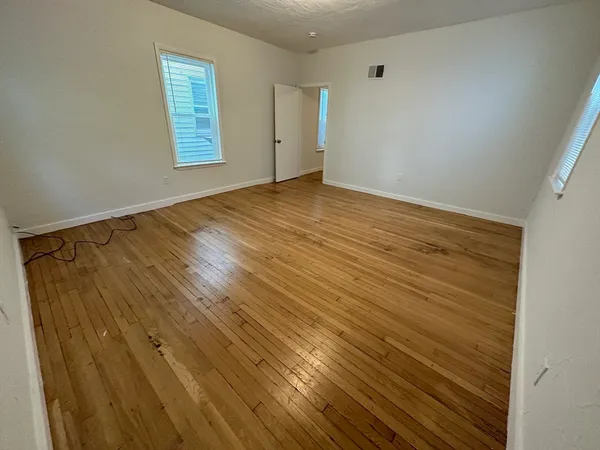 a view of an empty room with window and wooden floor