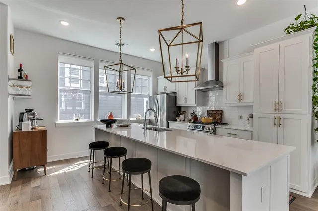 a kitchen with stainless steel appliances a sink a stove a refrigerator white cabinets and wooden floor