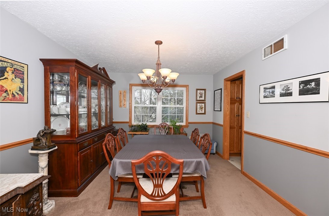 3305 Edington Road Akron, OH 44333 - Photo 10 of 46 Dining space with visible vents, a textured ceiling, baseboards, light colored carpet, and a chandelier