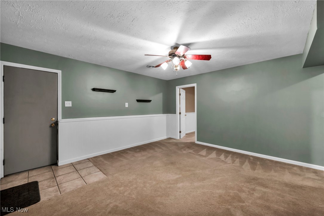 47655 Cooper Foster Park Road Amherst, OH 44001 - Photo 28 of 49 Carpeted spare room with a ceiling fan, a textured ceiling, a wainscoted wall, and tile patterned floors