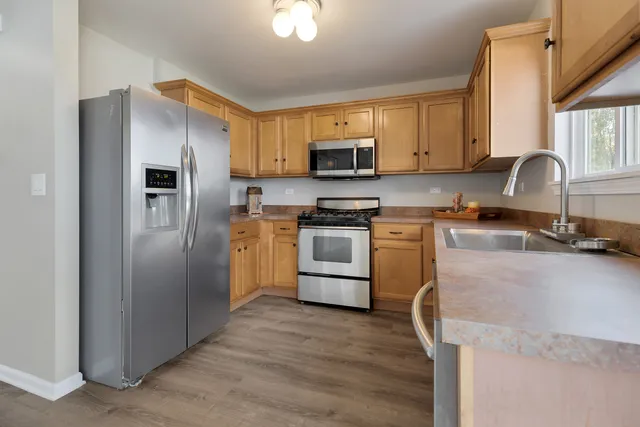 a kitchen with stainless steel appliances granite countertop a refrigerator a stove top oven a sink and dishwasher with wooden floor