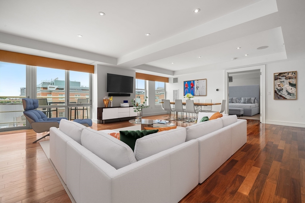 a living room with furniture floor to ceiling window hardwood floor and a flat screen tv