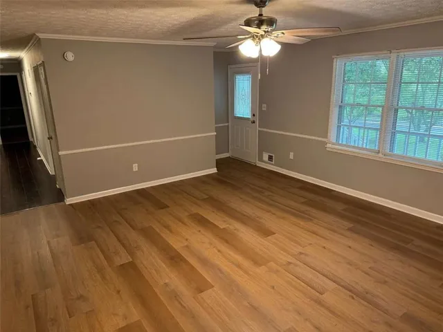 an empty room with wooden floor fan and windows