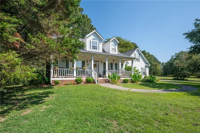 a view of a white house next to a yard with plants and trees