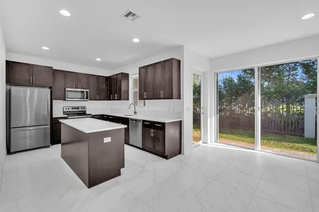 a large kitchen with kitchen island a large counter top stainless steel appliances and cabinets