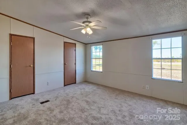 an empty room with chandelier fan and windows
