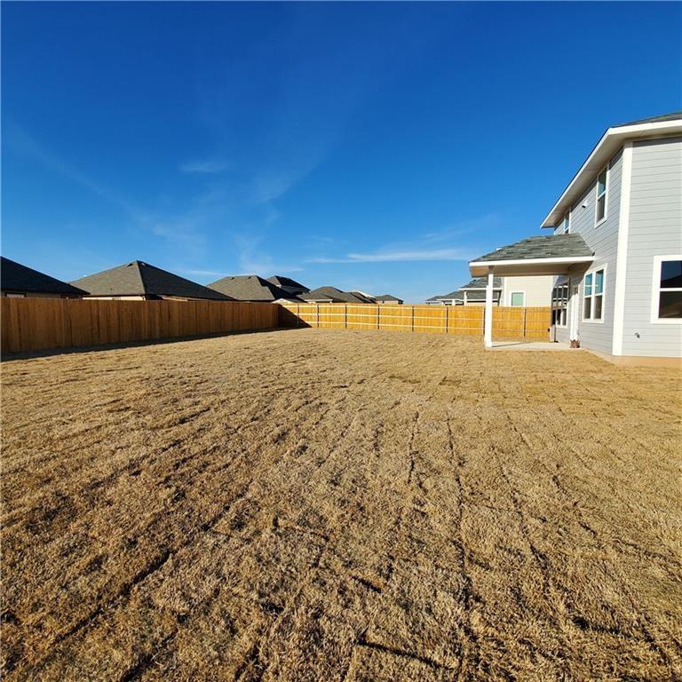 212 Lake Placid Run Elgin, TX 78621 - Photo 25 of 27 Expansive backyard featuring a full wood privacy fence, a covered patio with white columns, and a light gray siding exterior