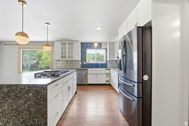 1410 Sumac Drive Logan, UT 84321 - Photo 3 of 28 Spacious kitchen featuring a large island with a built-in gas cooktop, white shaker-style cabinetry, dark stainless steel appliances, and wood-finish flooring