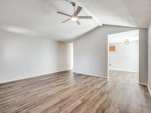 an empty room with wooden floor ceiling fan and windows