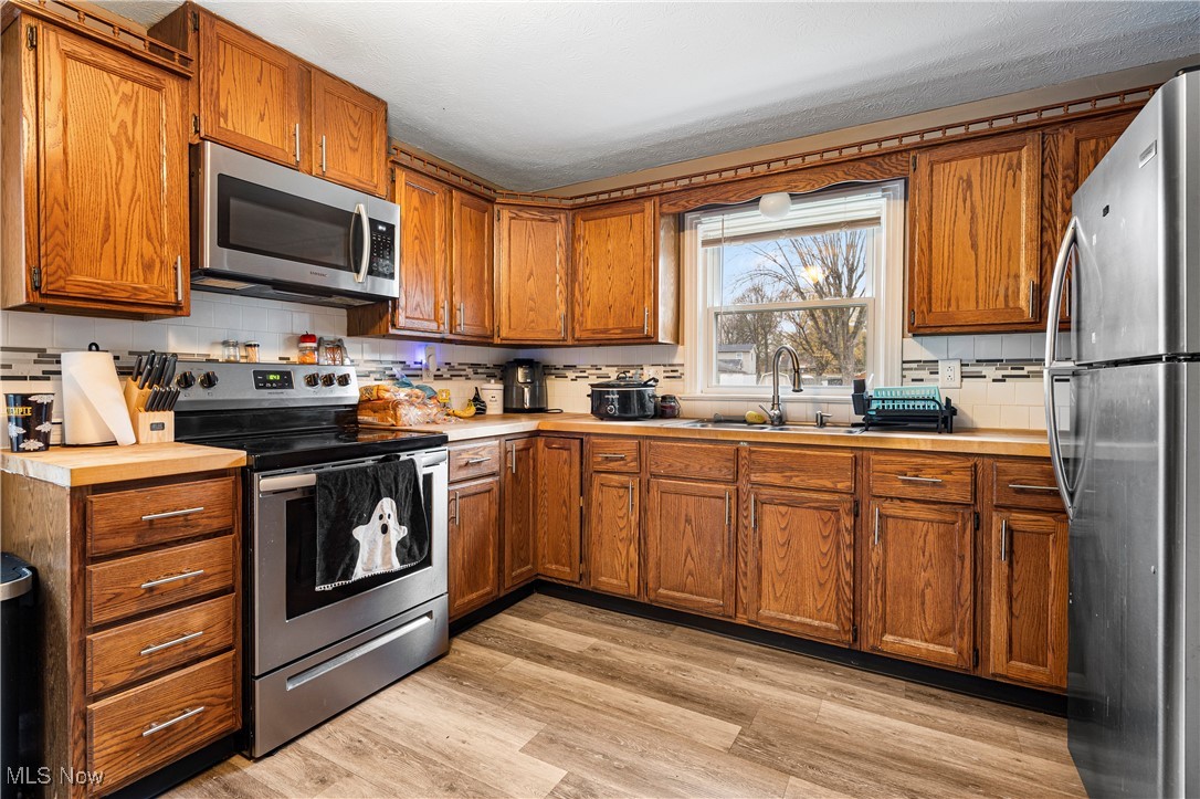 4617 17th Street Northwest Canton, OH 44708 - Photo 3 of 13 Kitchen featuring decorative backsplash, appliances with stainless steel finishes, brown cabinetry, and light wood finished floors
