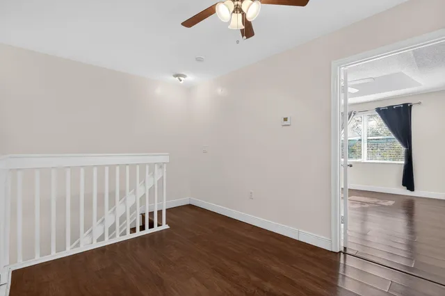a view of an empty room with wooden floor and a ceiling fan