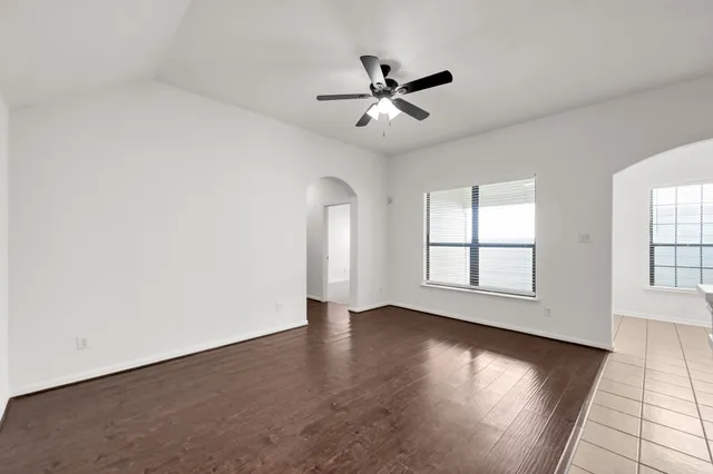 an empty room with wooden floor fan and windows