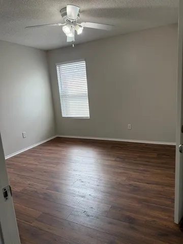 an empty room with wooden floor chandelier fan and windows