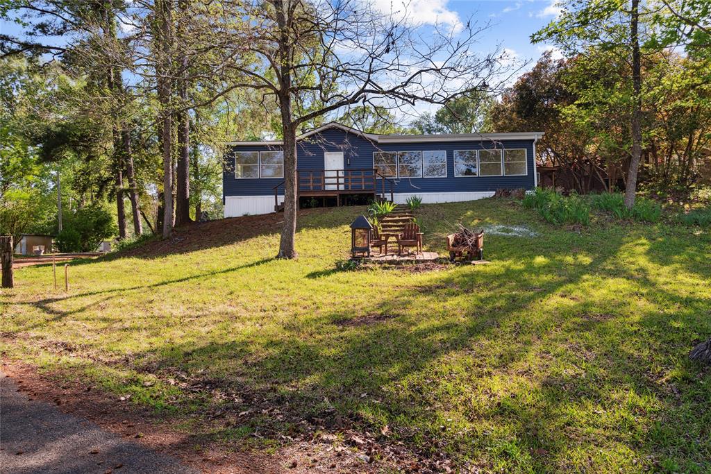 Wooded property featuring a blue-sided residence with white trim, a front deck, and a series of large windows