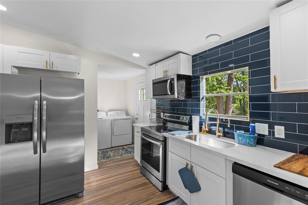 141 Mallard Road Ringgold, LA 71068 - Photo 8 of 33 Kitchen featuring wood-finish flooring, white cabinetry with gold-tone hardware, a stainless steel side-by-side refrigerator, a stainless steel range and built-in microwave, and a dark blue subway tile backsplash