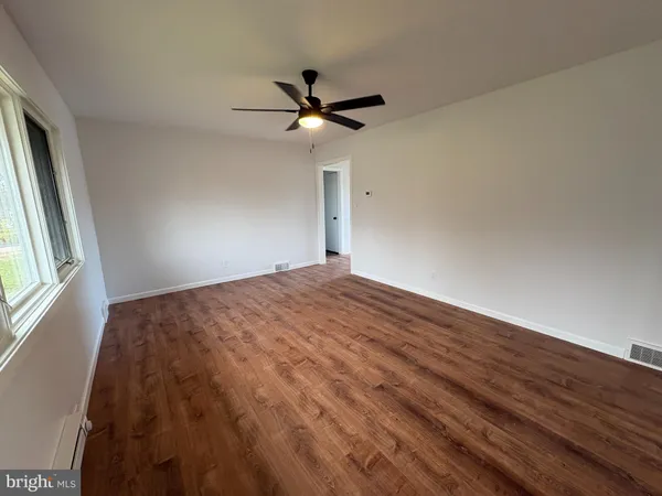 a view of a big room with wooden floor a ceiling fan and windows