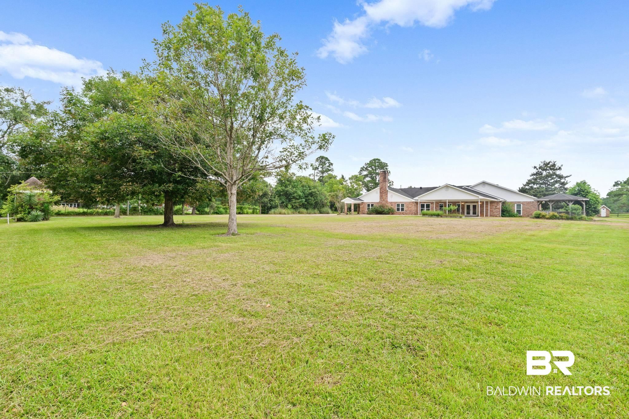 7540 2 Mile Road Irvington, AL 36544 - Photo 72 of 82 Expansive green space featuring a brick residence with multiple windows, a covered patio, and a separate gazebo structure