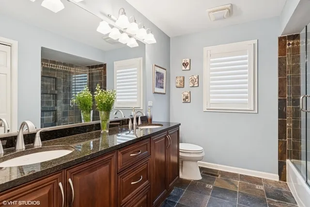a bathroom with a granite countertop sink a toilet a mirror and shower