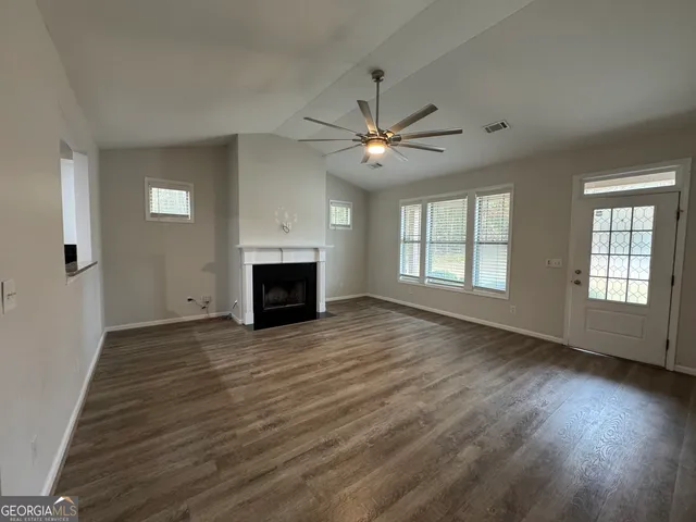 an empty room with wooden floor fireplace and windows