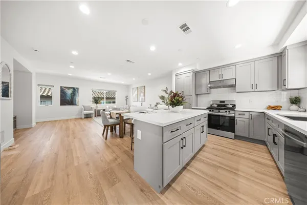 a large kitchen with stainless steel appliances granite countertop a large counter top a sink a stove and chairs with wooden floor