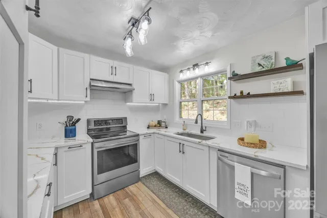 a kitchen with stainless steel appliances granite countertop a sink dishwasher stove and white cabinets with wooden floor