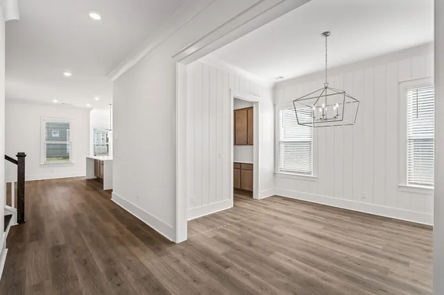 a view of an empty room with wooden floor kitchen view and a window