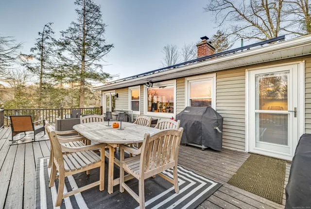 a view of a roof deck with table and chairs a barbeque with wooden floor and fence