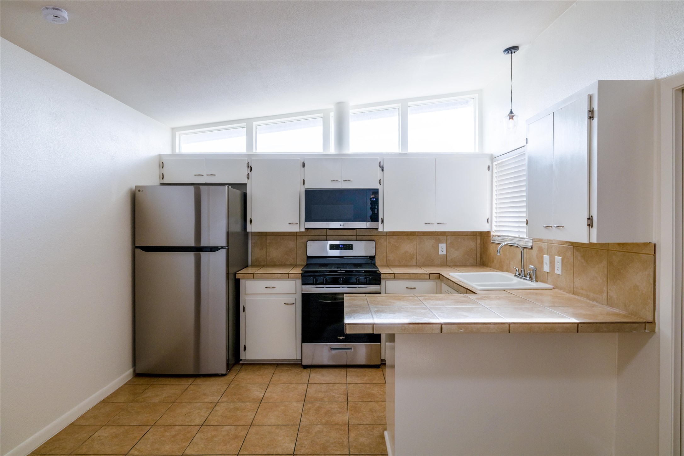 4304 Scottsdale Road Austin, TX 78721 - Photo 4 of 18 Kitchen featuring stainless steel appliances, white cabinets, a peninsula, decorative backsplash, and tile counters