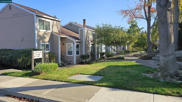 a view of a white house next to a yard with big trees and plants