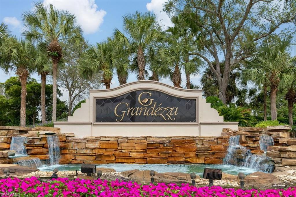 20117 Seadale Court Estero, FL 33928 - Photo 34 of 34 Prominent Grandezza community signage, tiered stone waterfalls, vibrant pink flowering groundcover, mature palm trees, and lush green foliage